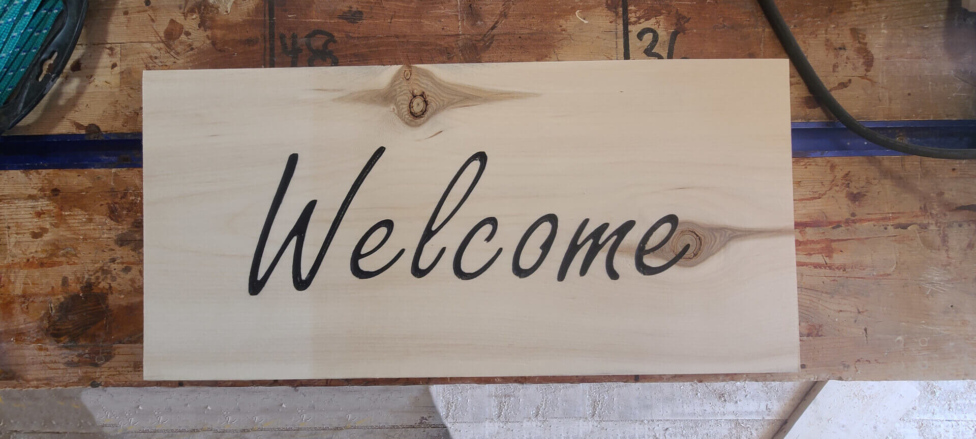 Image of a wooden welcome sign complete with a couple knots.